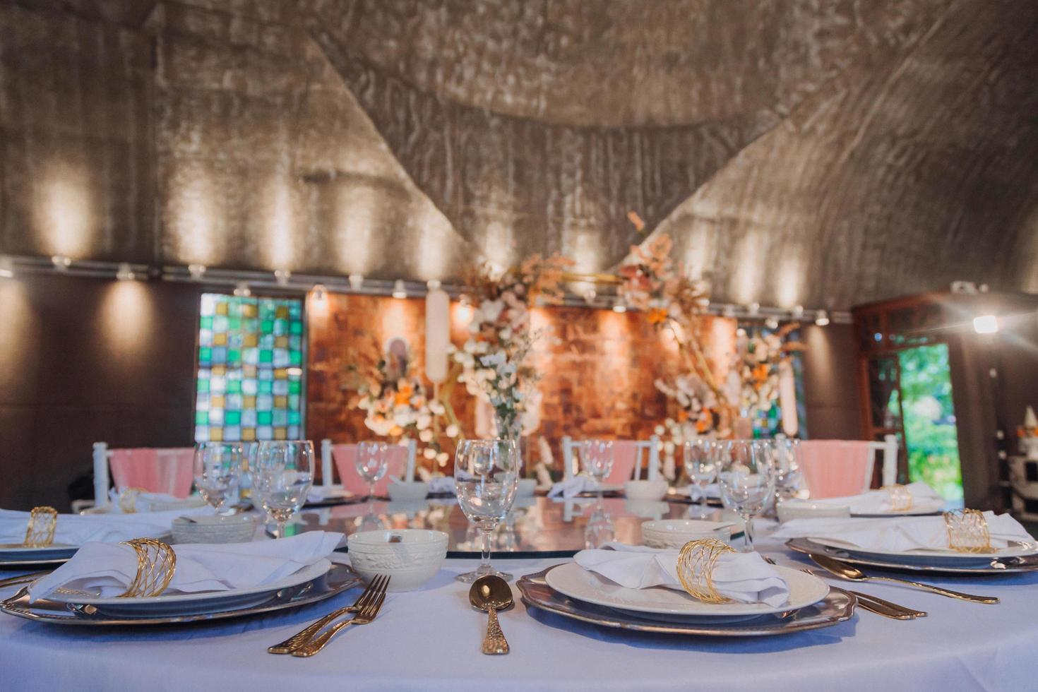 bloemstuk voor zomerhuwelijk, gemaakt van rozen en groene takken op een eettafel in het restaurant. , glas en borden in het restaurant buiten op een winderige dag met filmkorreleffect foto