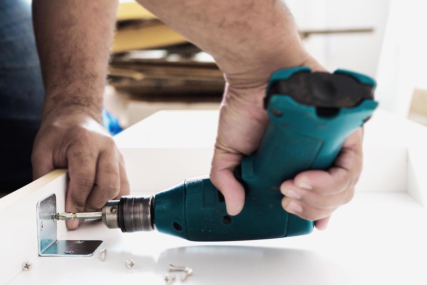 man werkt met meubelmontage met behulp van elektrische schroevendraaier in nieuwe huisinstallatie - technicus ter plaatse werkt met handgereedschapconcept foto