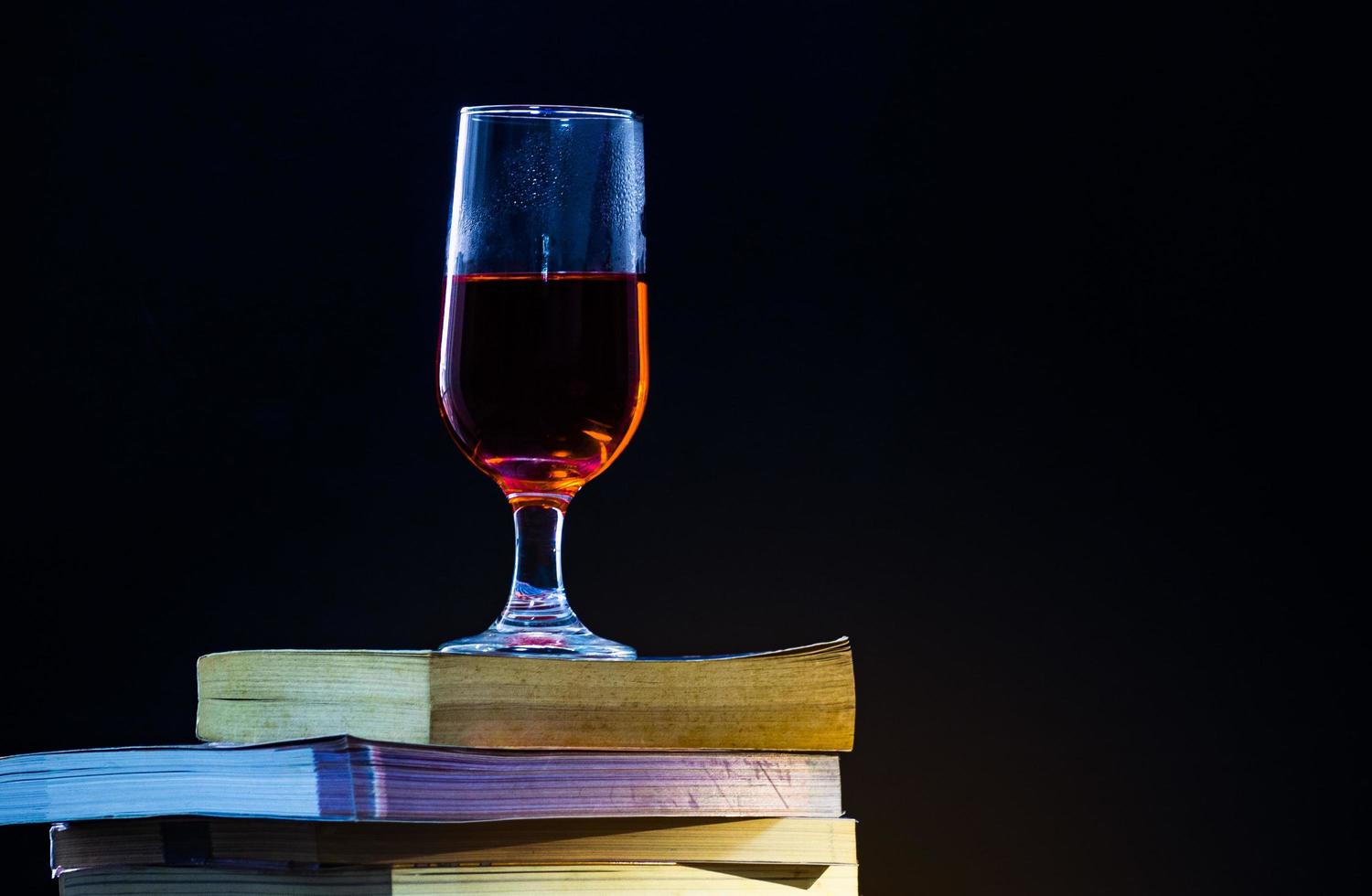 oude boeken overlappen elkaar op een zwarte achtergrond en met gedimd licht een glas rode wijn erop. foto