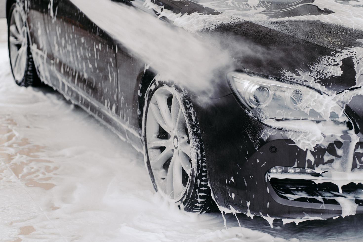 zwarte auto gewassen door hoge druk van water en zeep bij carwash. schoonmaak dienstverleningsconcept. zelfbediening autowasstation foto