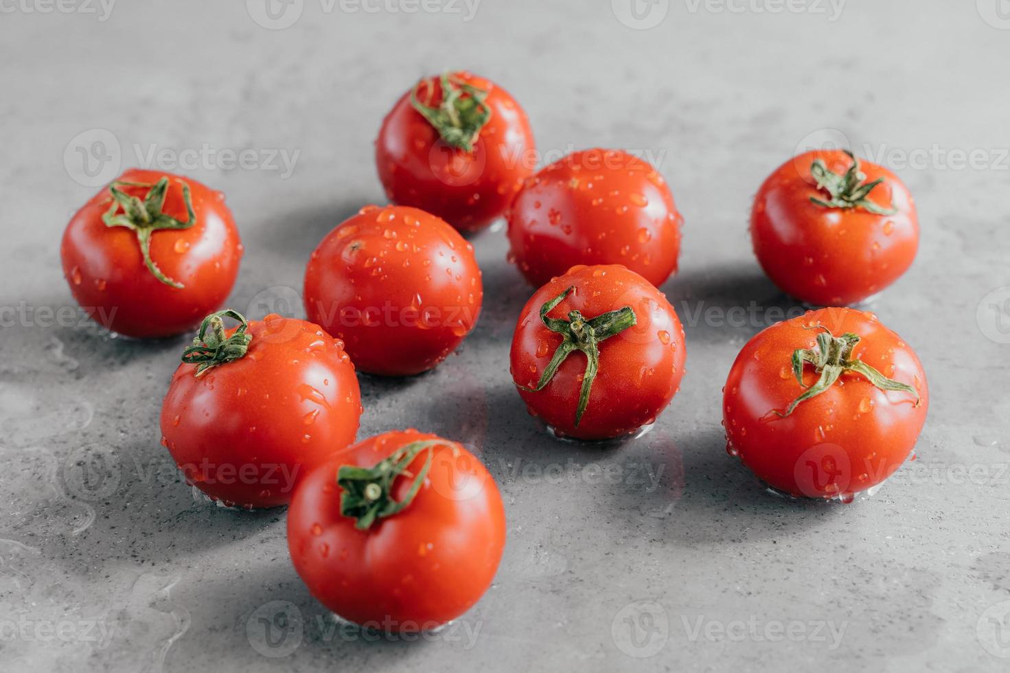 macro-opname van rijpe tomaten met druppels dauw die net op de tuin zijn geoogst. biologisch voedselconcept. kerstomaatjes op grijze achtergrond foto