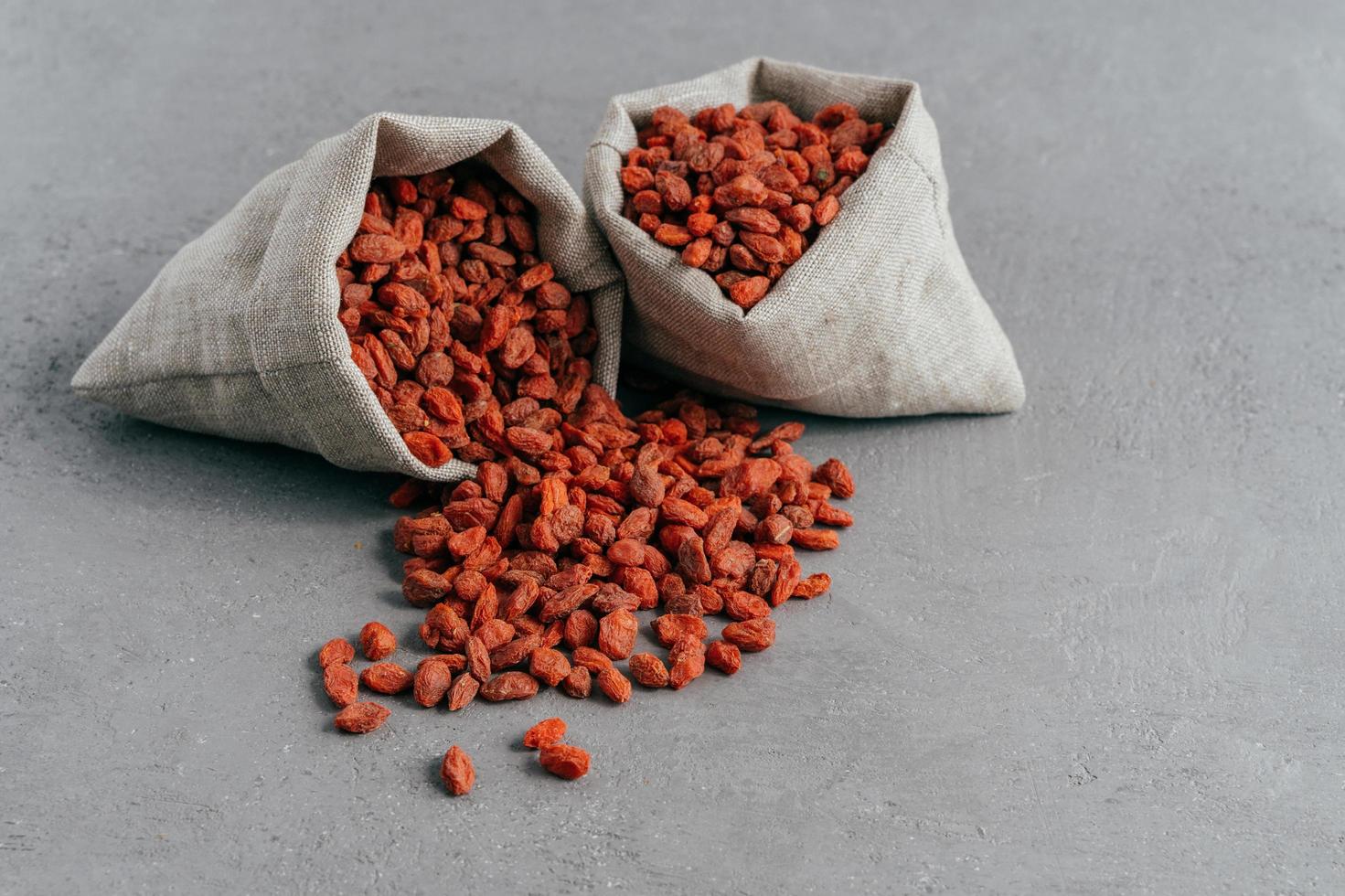 rauwe rode biologische goji-bessen in kleine rustieke zakken en verspreid op een grijze achtergrond. voedsel en voedingsconcept. wolfsbessen om te eten foto