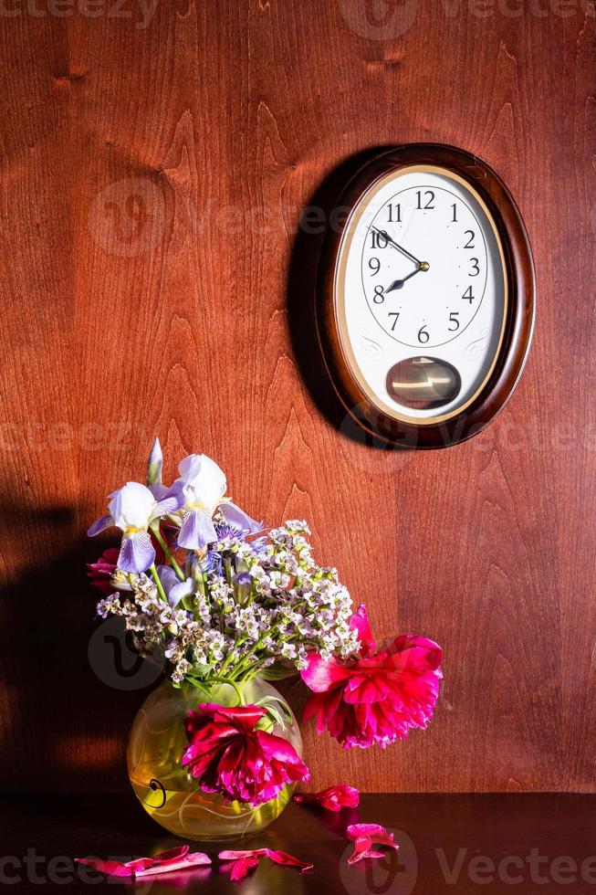 wandklok en verwelkte bloemen in vaas op bruin foto