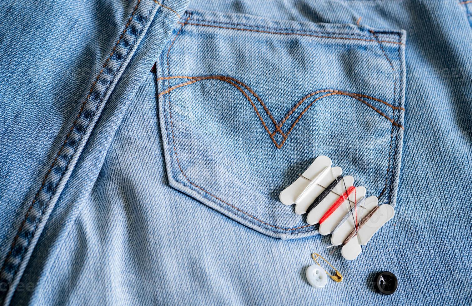 hotel naaisetje op jeans. kleine draagbare draadreparatie-noodset met naalden, knopen, draden en veiligheidsspelden voor hotel, thuis en op reis. eco naaisetje. hotel voorzieningen. kleding reparatieset. foto