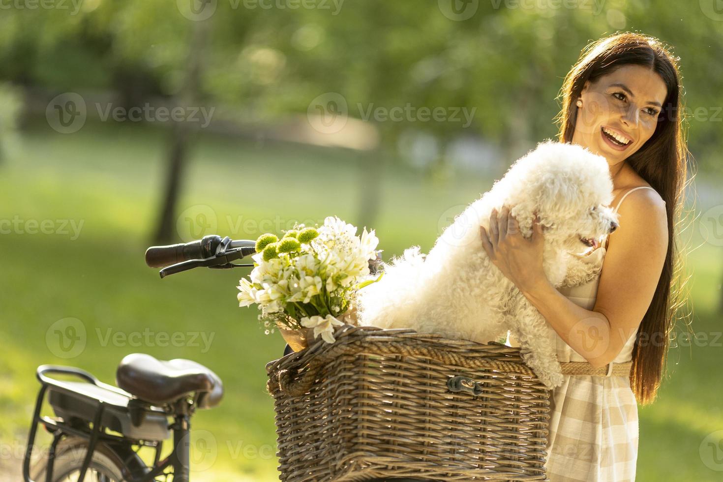 jonge vrouw met witte bichon frise hond in de mand van elektrische fiets foto
