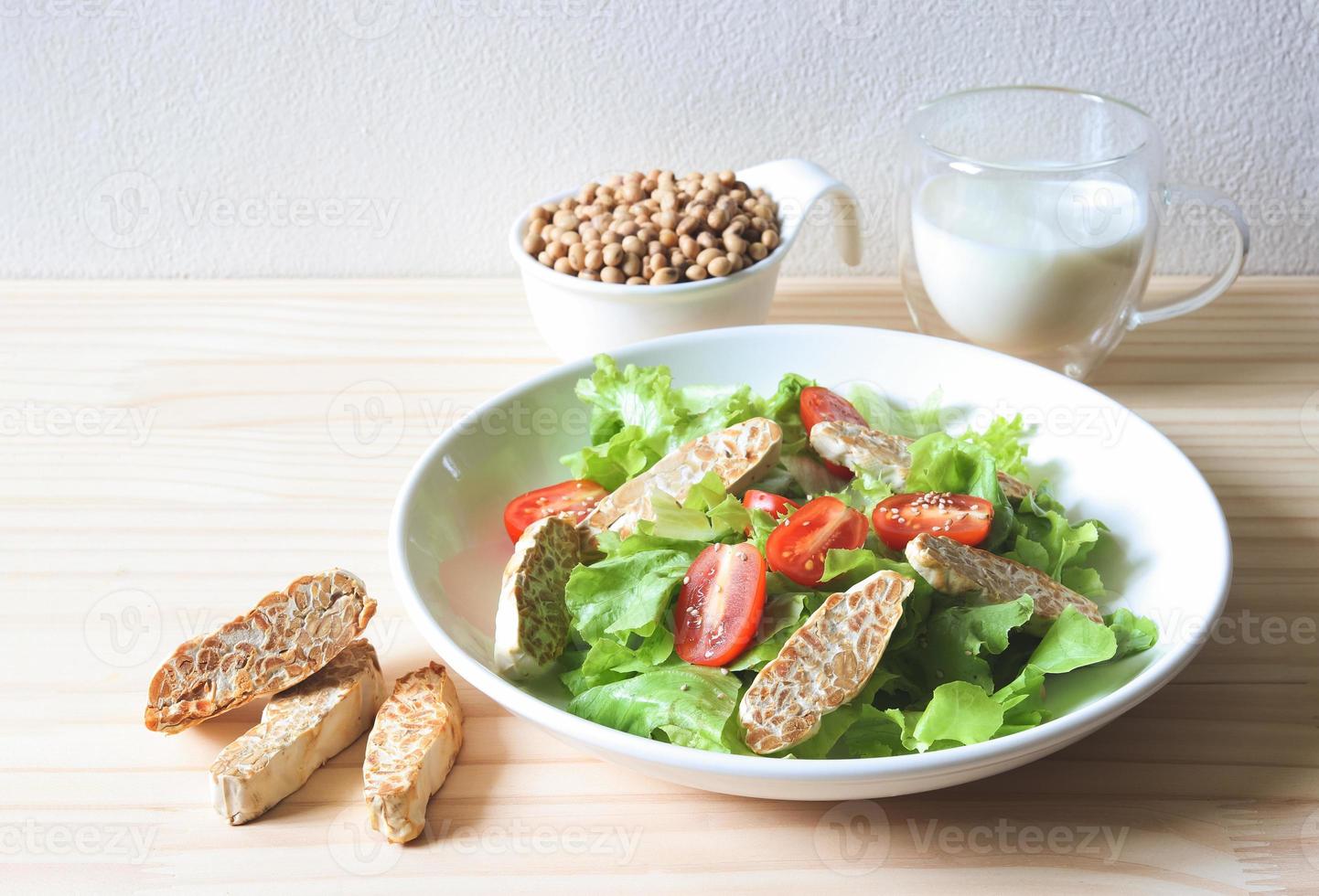 tempeh in saladeschotel, sojabonenzaden in witte kom en sojamelk op houten tafel, producten van sojabonen. foto