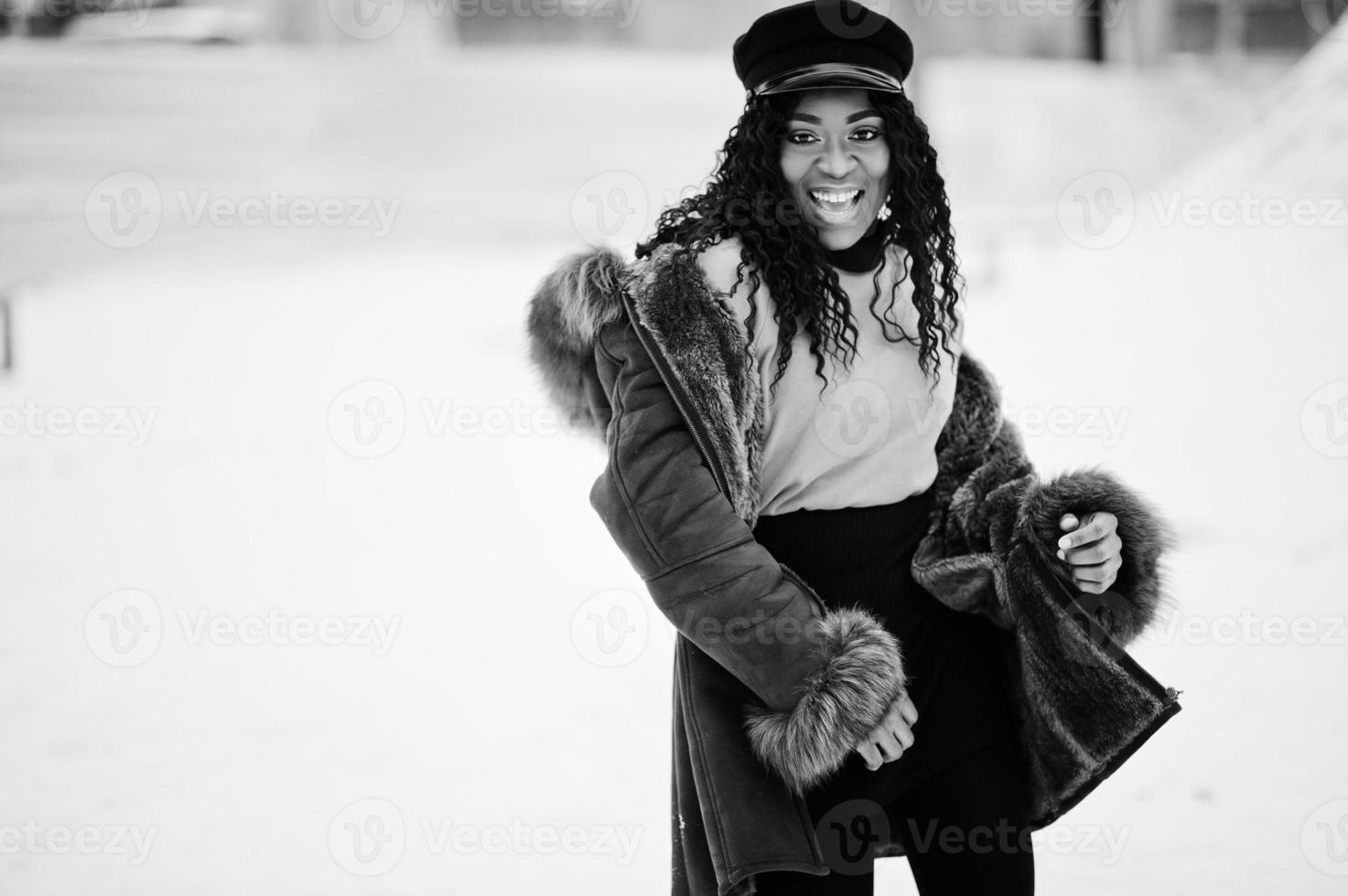 Afro-Amerikaanse vrouw in schapenvacht jas en pet gesteld op winterdag tegen besneeuwde achtergrond. foto