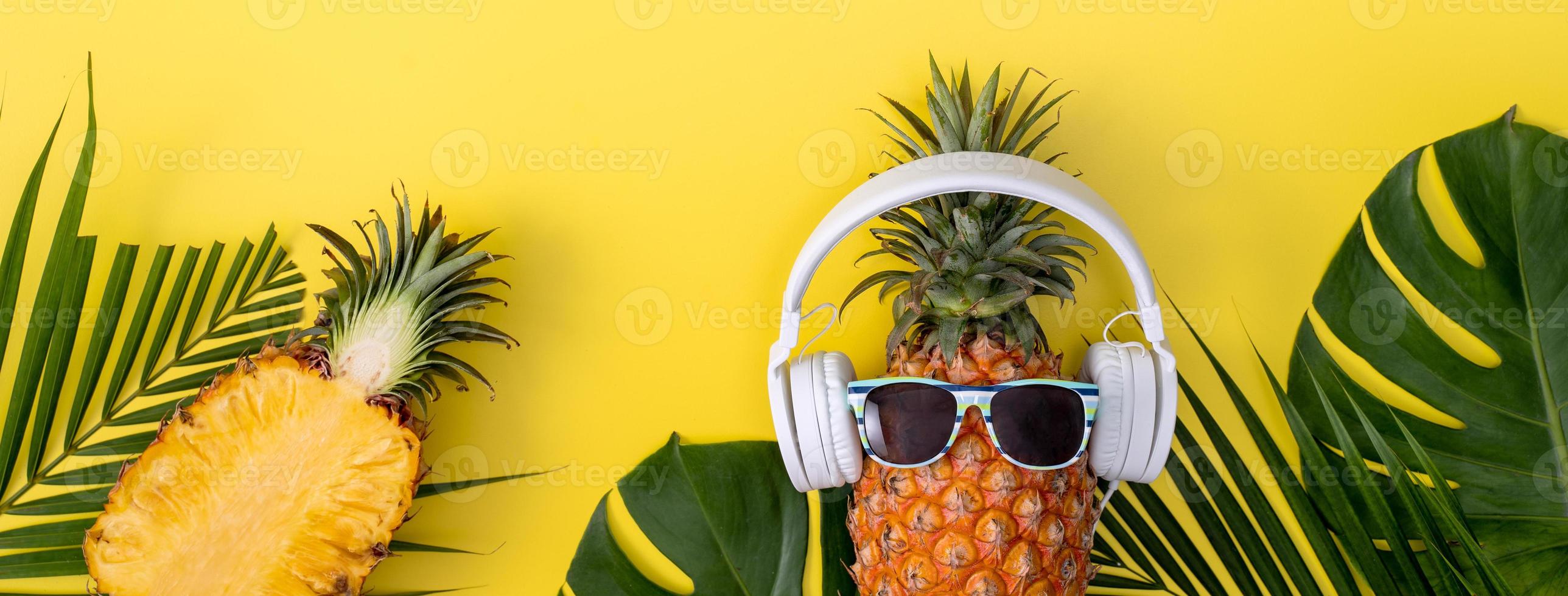 grappige ananas met witte hoofdtelefoon, luister muziek, geïsoleerd op gele achtergrond met tropische palmbladeren, bovenaanzicht, plat ontwerpconcept. foto