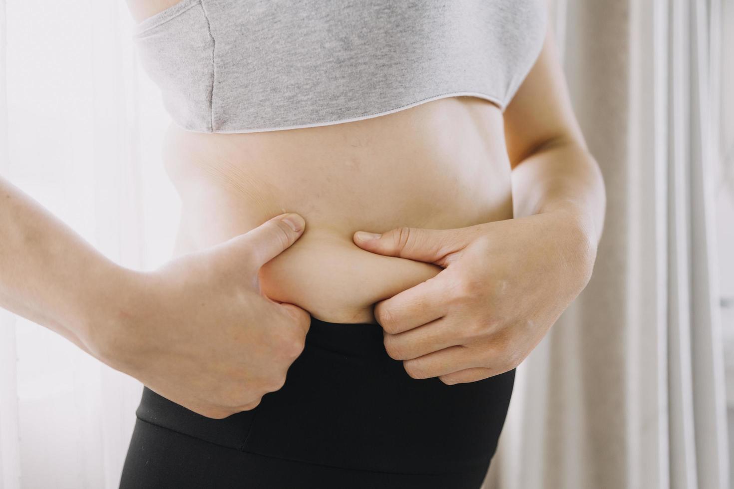 mooie dikke vrouw met meetlint ze gebruikt haar hand om het overtollige vet dat op een witte achtergrond is geïsoleerd uit te knijpen. ze wil afvallen, het concept van chirurgie en vet afbreken onder de foto