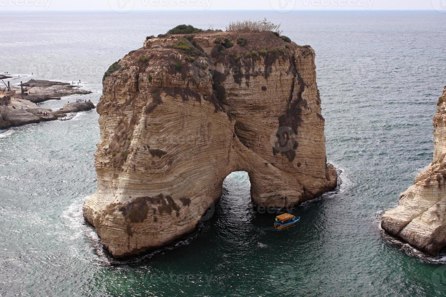 een kleine boot passeert een grote rots aan de kust van beiroet, libanon foto