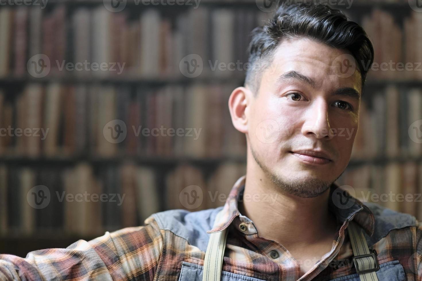 man met bedachtzame uitdrukking met bretels en een geruit overhemd in een bibliotheek foto