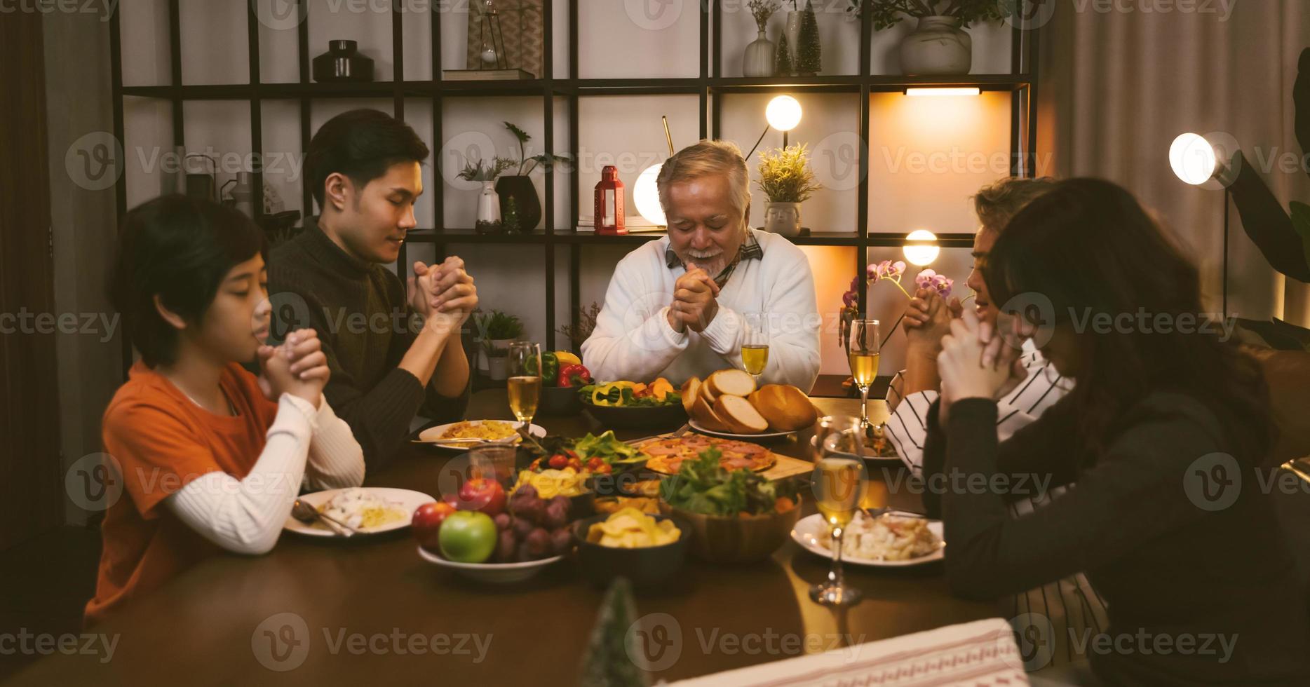 aziatische grote familie die ogen sluit en handen bidt bij het zeggen van genade bidden voordat ze thuis gaan eten foto