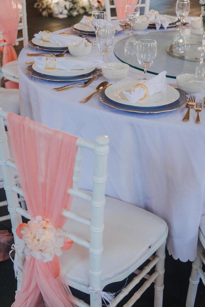 bloemstuk voor zomerhuwelijk, gemaakt van rozen en groene takken op een eettafel in het restaurant. , glas en borden in het restaurant buiten op een winderige dag met filmkorreleffect foto