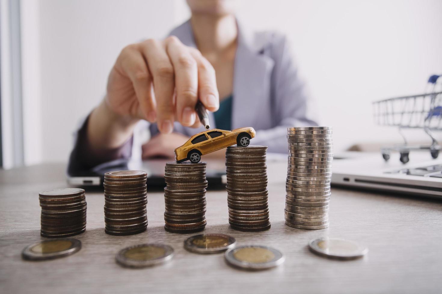 close-up van de hand die munt op stapelmunten zet om geld te besparen. geld inzamelen om een nieuwe auto, sparen en autoleningconcept te kopen. plat leggen foto