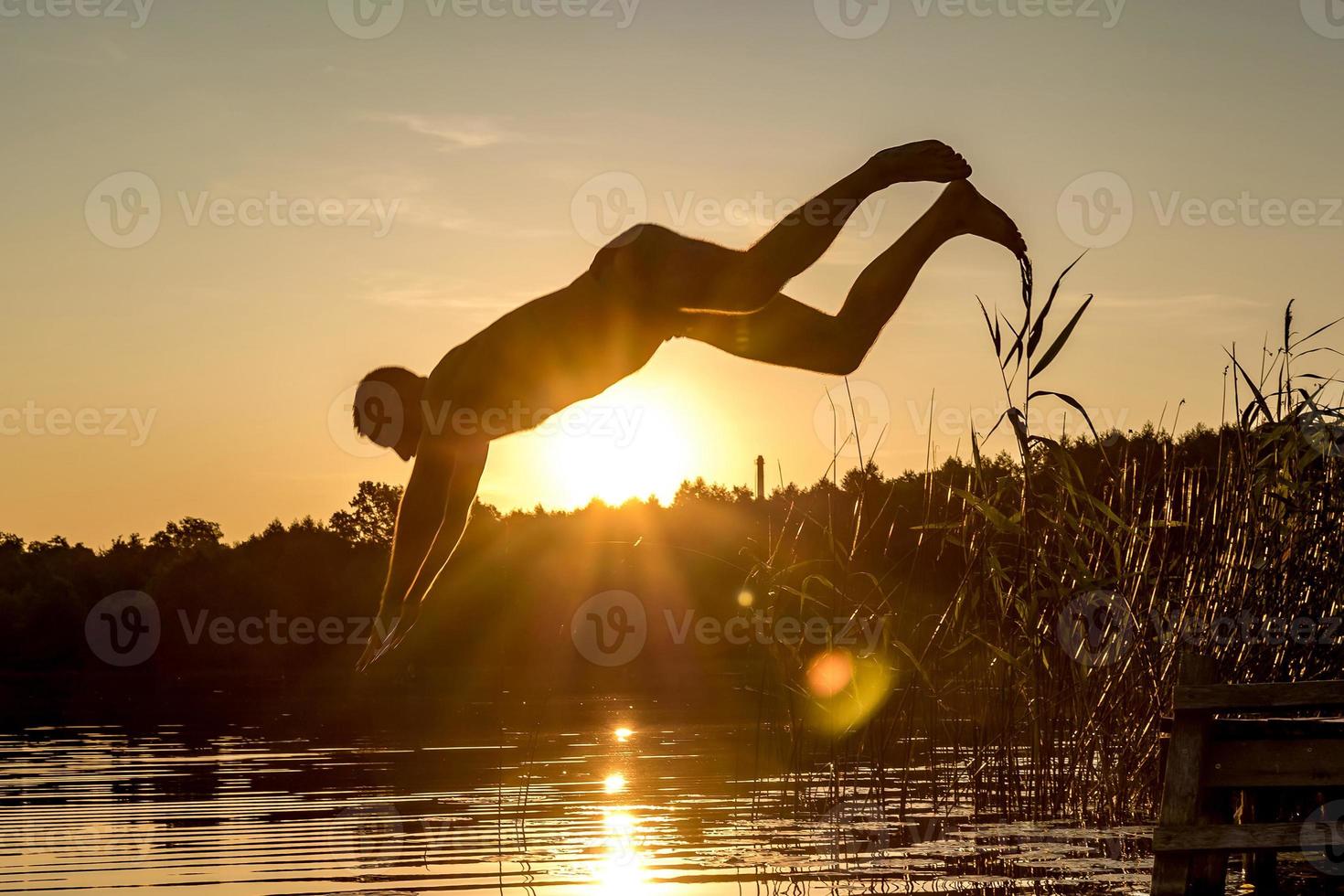 man duikt in het water van het meer bij zonsondergang foto