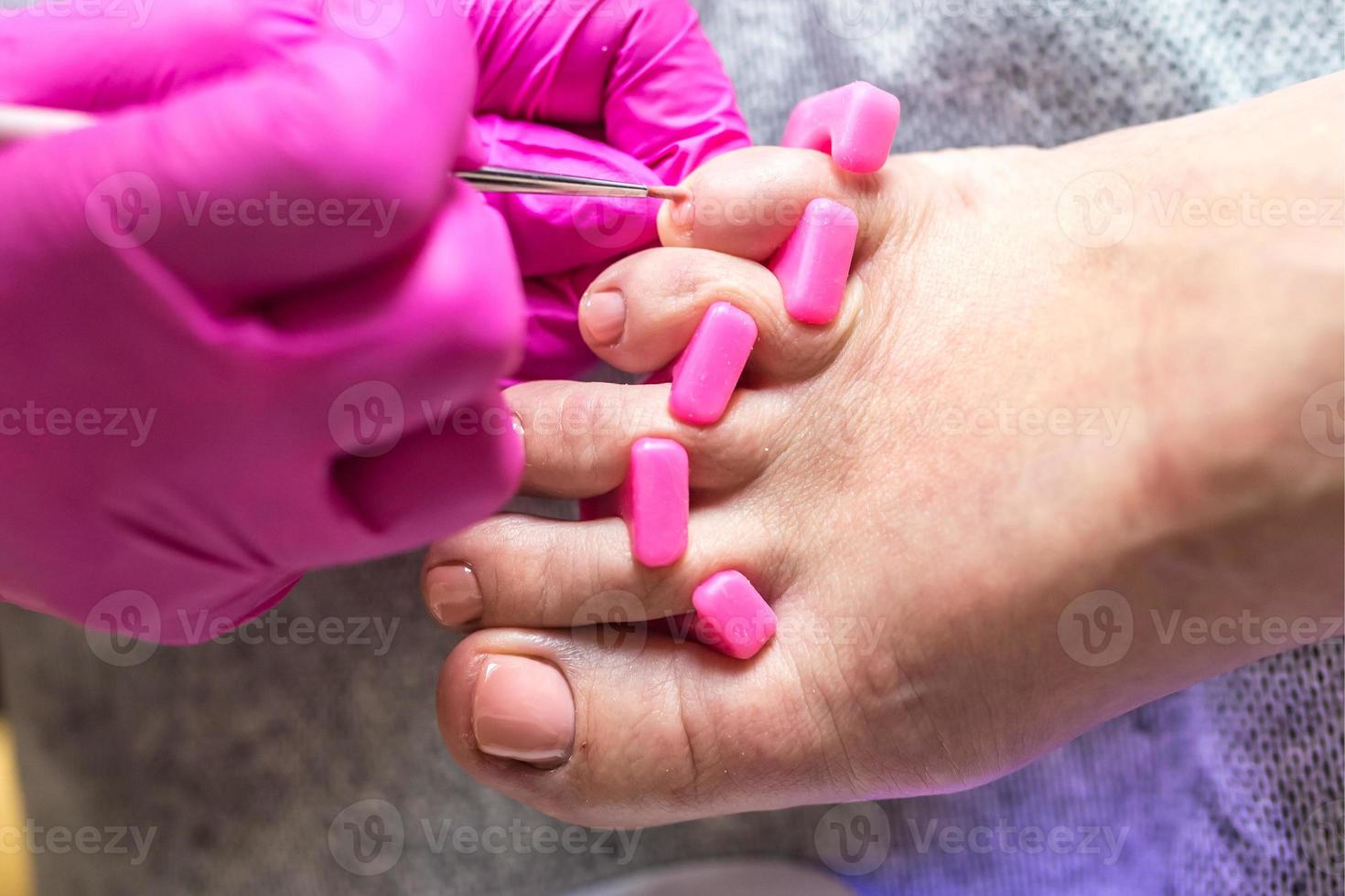 pedicure meester in roze handschoenen snijdt de nagelriem en schellak teennagels in de pedicure salon met behulp van boor. professionele pedicure in cosmetologiekliniek. hygiëne voor voeten in schoonheidssalon. foto