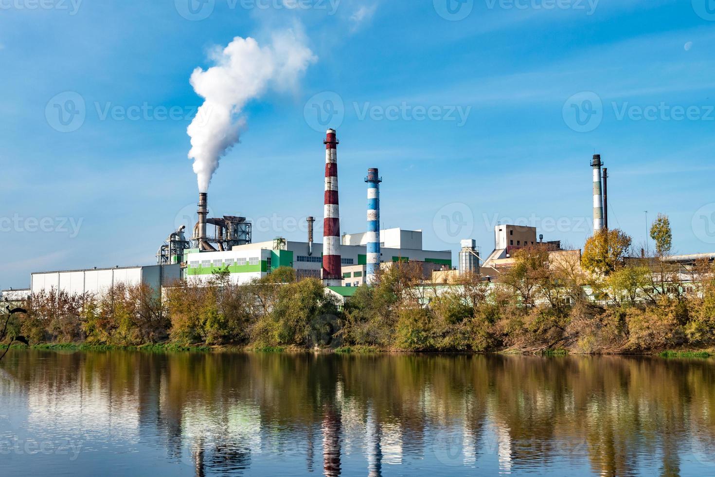 pijpen van houtbewerking onderneming plant zagerij in de buurt van rivier. luchtvervuiling concept. industrieel landschap milieuvervuiling afval van thermische elektriciteitscentrale foto