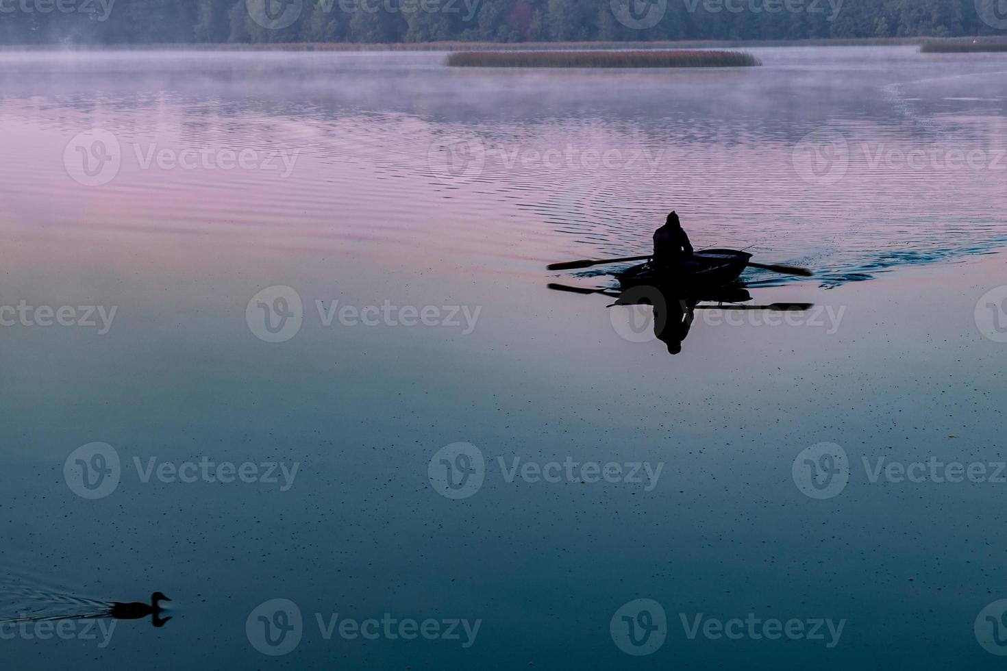 silhouet van de mens in een boot in de vroege ochtend. roze dageraad met eenden foto