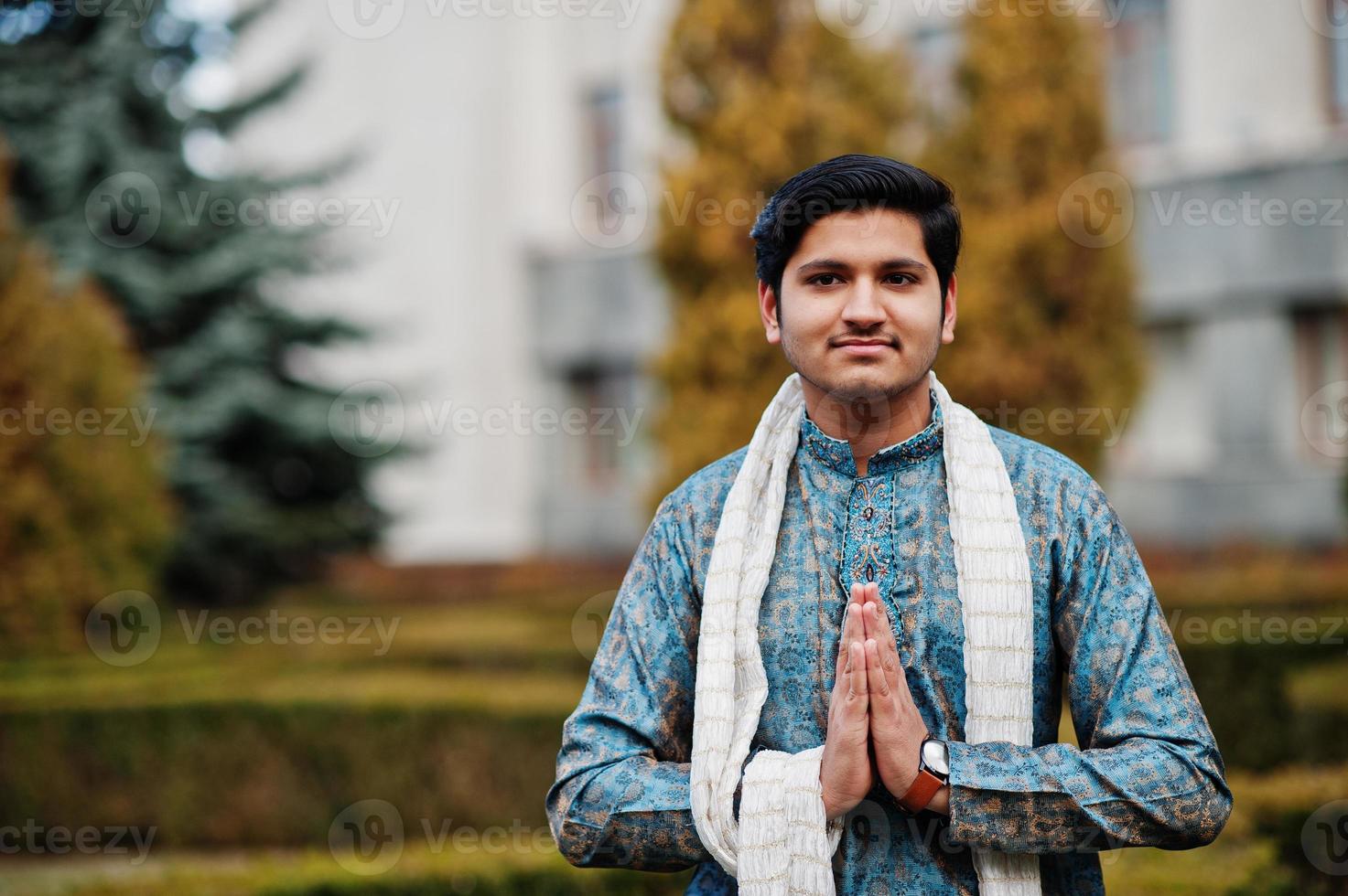 indiase man draagt traditionele kleding met witte sjaal buiten tegen groene struiken in het park, toon namaste handen teken. foto