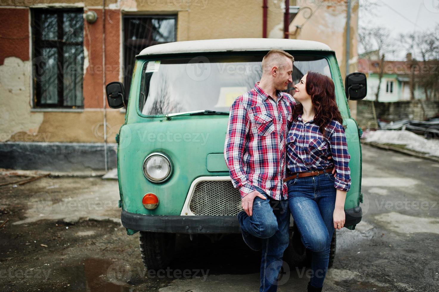 stijlvolle paar slijtage op geruite shirt verliefd samen tegen oude minivan. foto