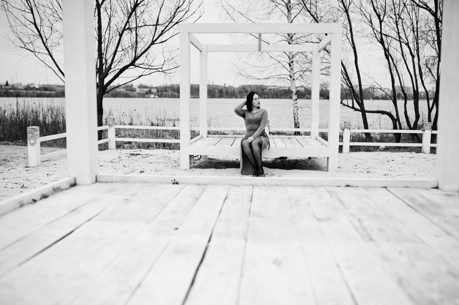 portret van brunette meisje in grijze jurk zit op witte houten constructie. foto