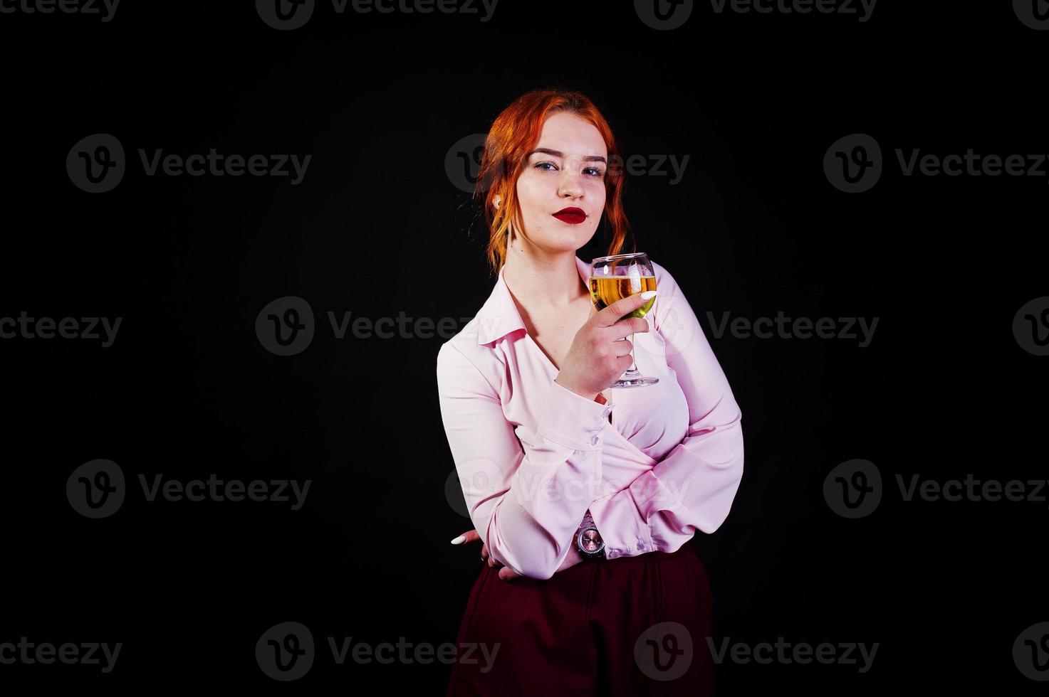 prachtige roodharige meisje in roze blouse en rode rok met glas wijn bij de hand geïsoleerd op zwart. foto