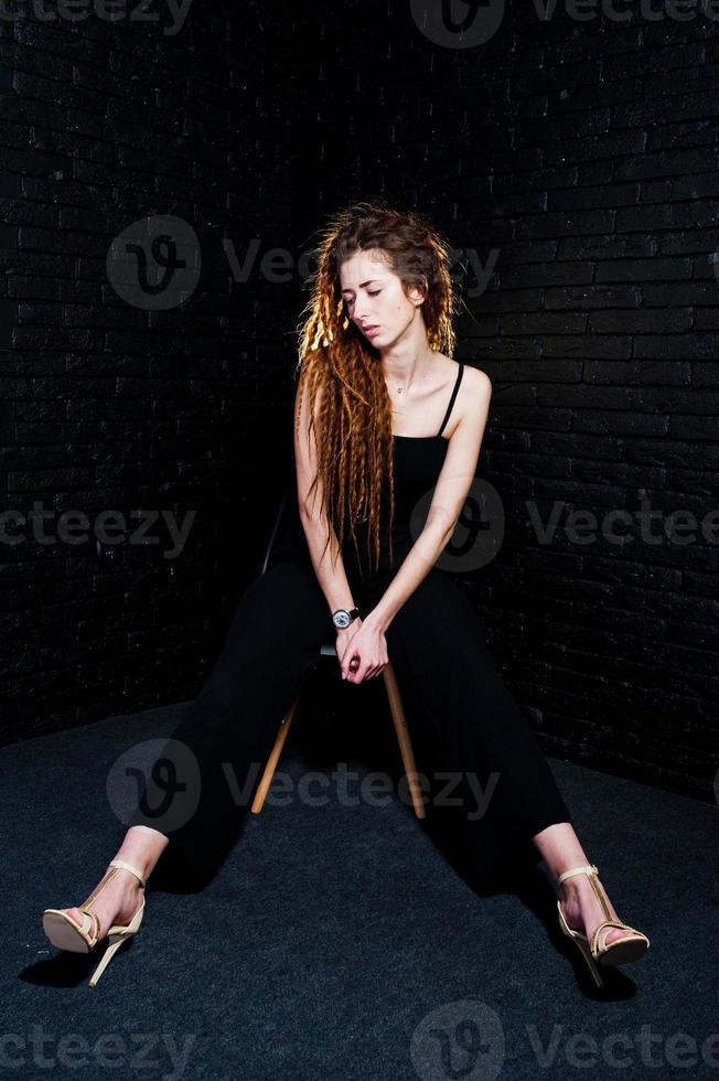 studio shoot van meisje in het zwart op stoel met dreadlocks op baksteen achtergrond. foto