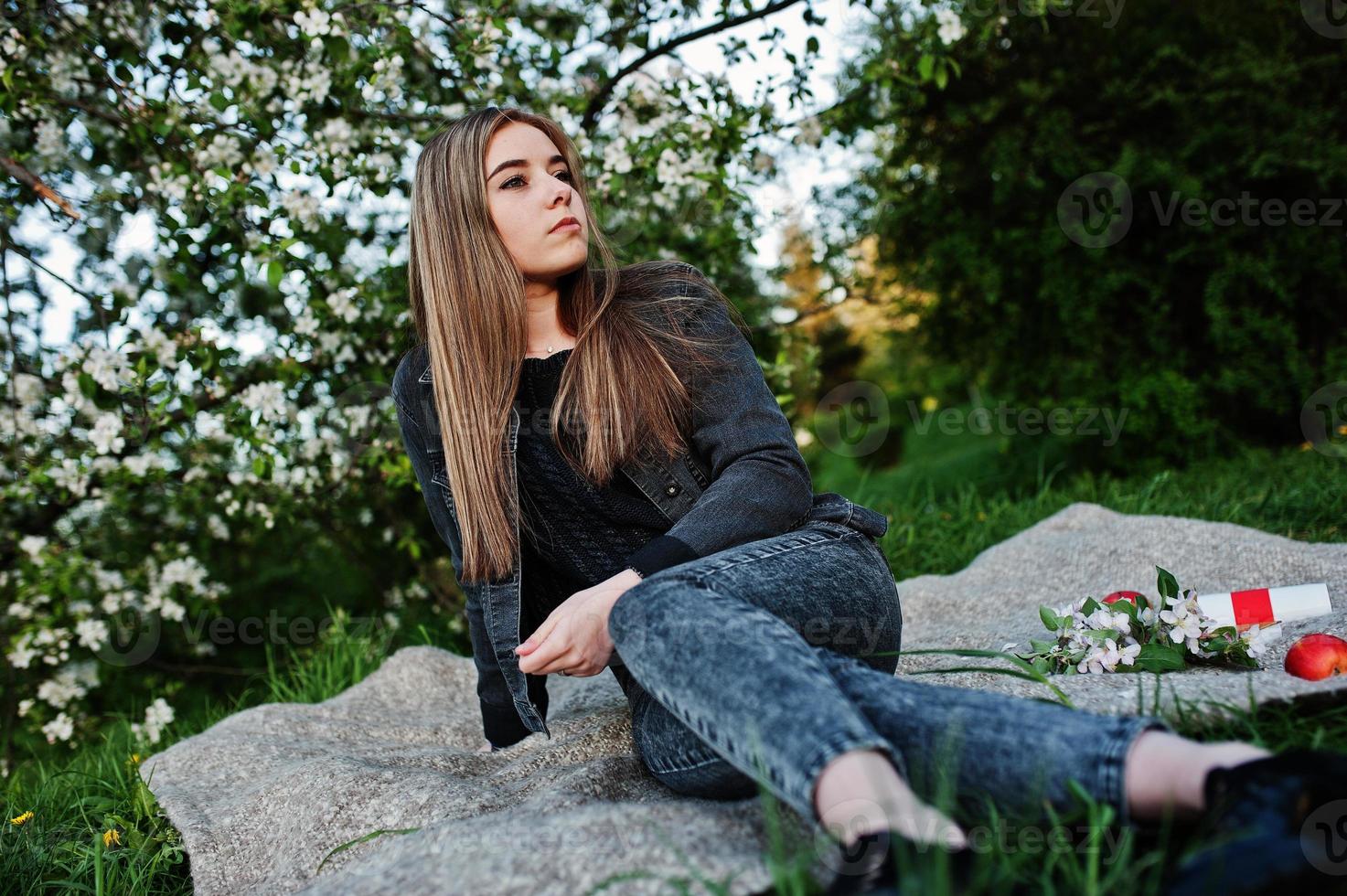 jonge brunette meisje op jeans zittend op plaid tegen lente bloesem boom. foto