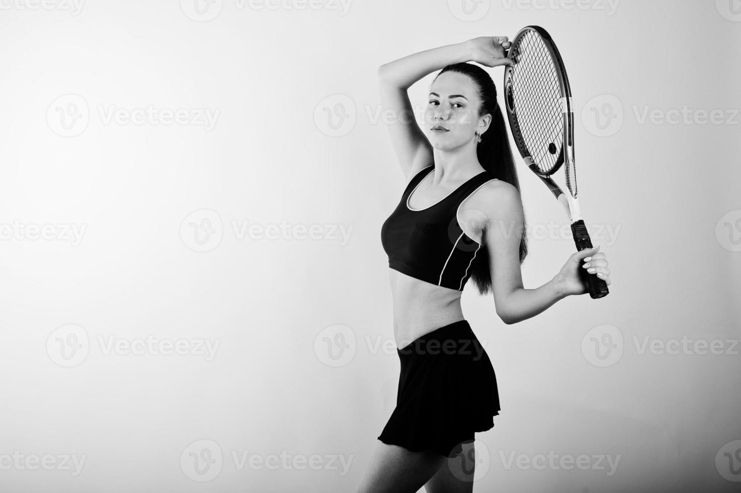 zwart-wit portret van een mooie jonge vrouw in sportkleding die een tennisracket vasthoudt terwijl hij tegen een witte achtergrond staat. foto