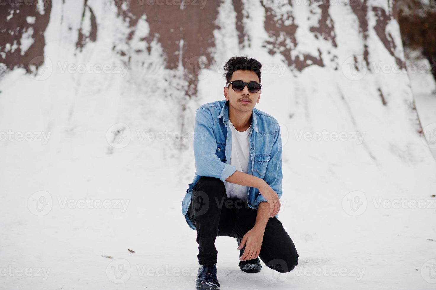 casual jonge Indiase man in spijkerbroek shirt en zonnebril poseerde op winterdag. foto