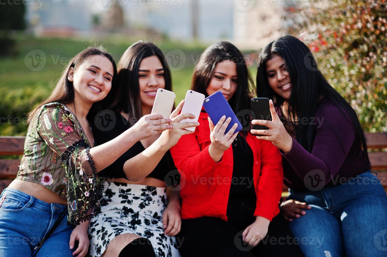 groep van vier gelukkige en mooie latino-meisjes uit ecuador poseerden op straat en kijken naar mobiele telefoons. foto