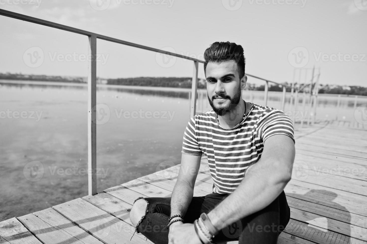 knappe lange arabische baard man model op gestript shirt poseerde buiten op de pier van het meer. modieuze Arabische man. foto