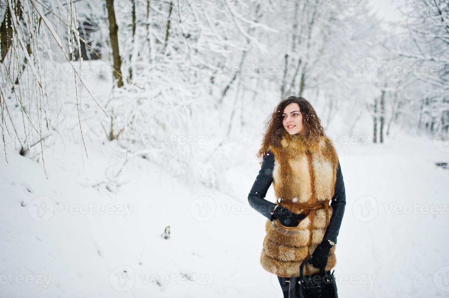 elegantie krullend meisje in bontjas en handtas in besneeuwde forest park in de winter. foto