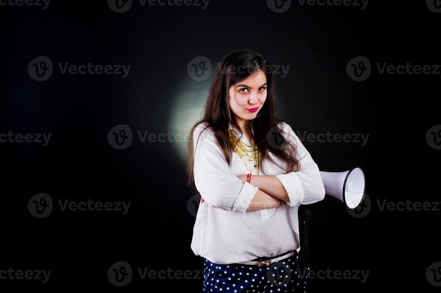 portret van een jonge vrouw in blauwe broek en witte blouse poseren met megafoon in de studio. foto