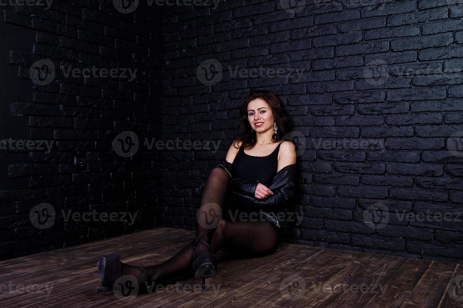 studioportret van sexy donkerbruin meisje in zwart leerjasje tegen bakstenen muur. foto