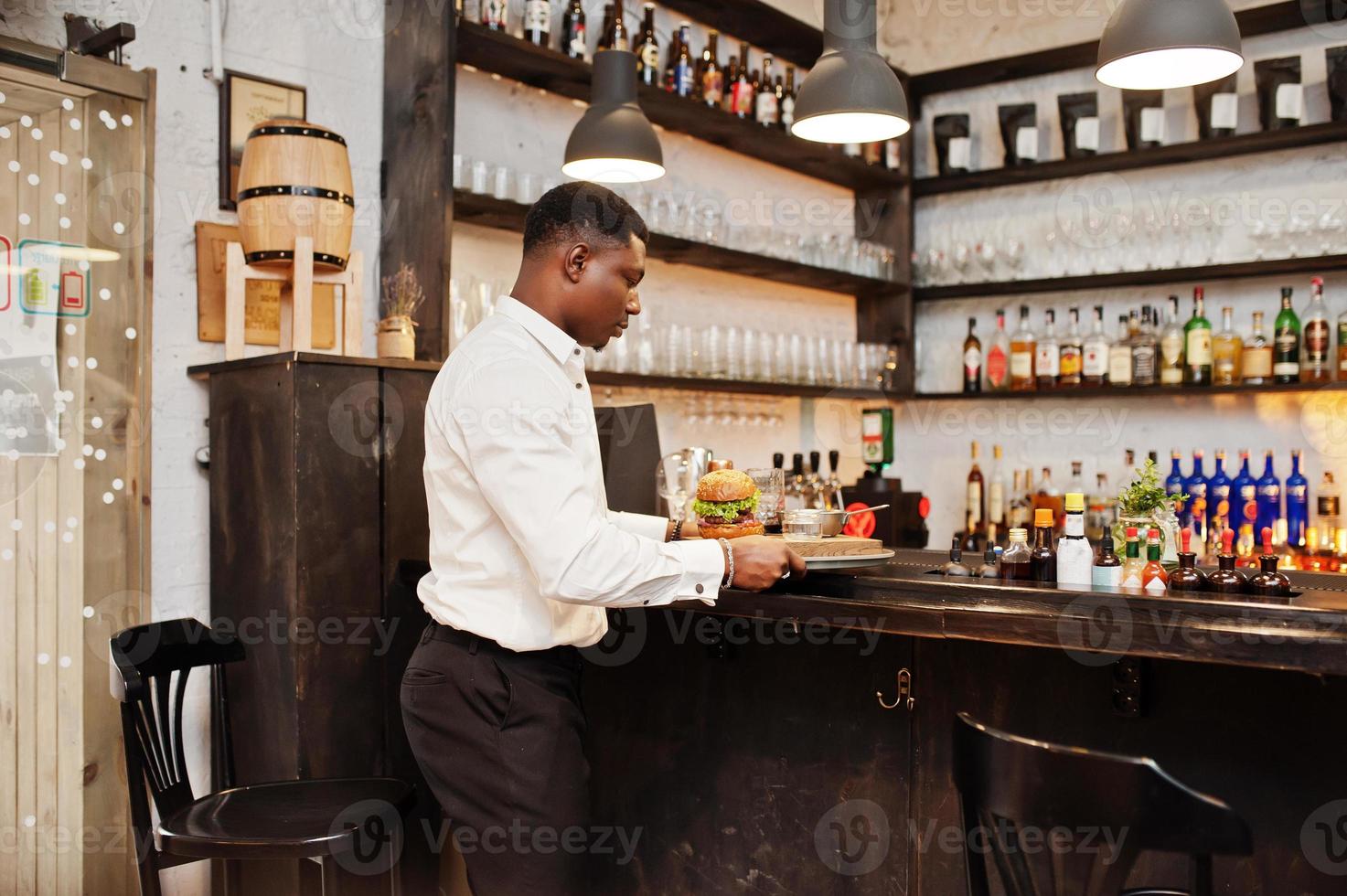 jonge Afro-Amerikaanse ober man houdt dienblad met hamburger aan de bar van het restaurant. foto