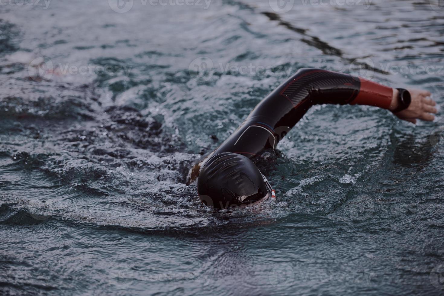 triatlonatleet die op meer in zonsopgang zwemt die wetsuit draagt foto