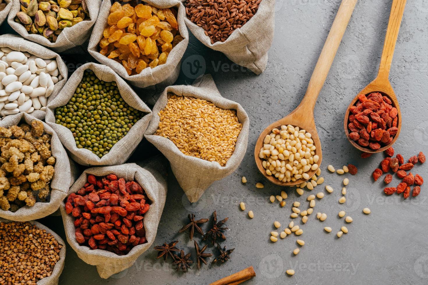 veeteelt en voeding concept. bovenaanzicht van verschillende bonen en kleurrijk gedroogd fruit verpakt in kleine jutezakken. houten lepel met ingrediënten foto