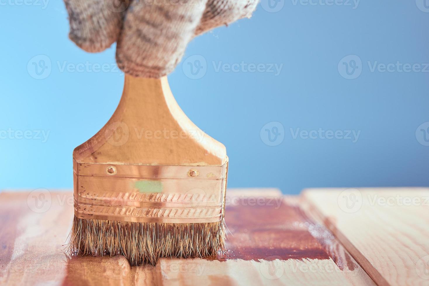 houten vloer schilderen met beschermende vernis op een blauwe achtergrond. hand in grijze werkhandschoen schilderen houten oppervlak. foto