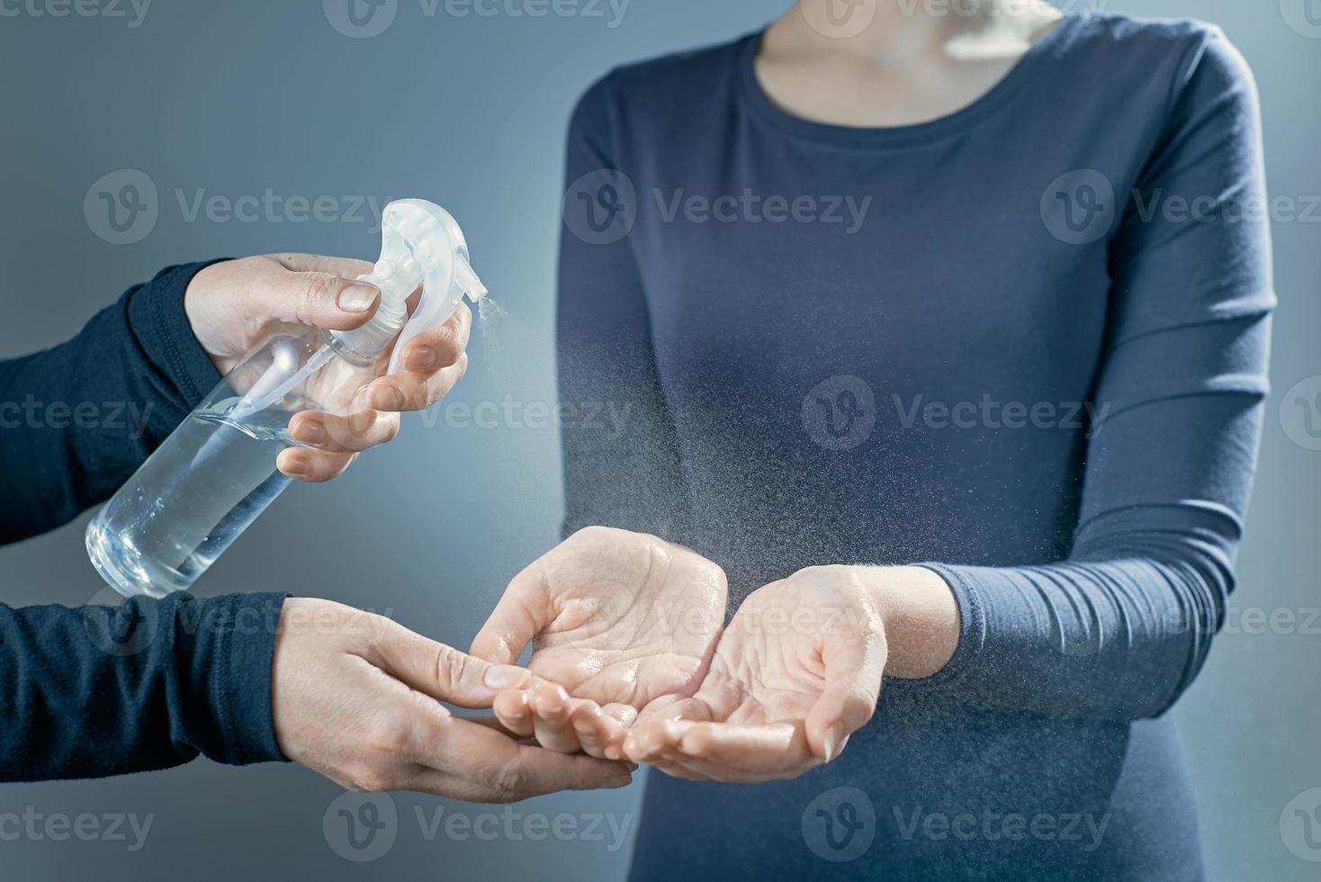 een moeder behandelt de handen van haar dochter met ontsmettingsmiddel. vrouwenhanden worden behandeld met een ontsmettingsmiddelmeisjeshanden op een grijze achtergrond. foto