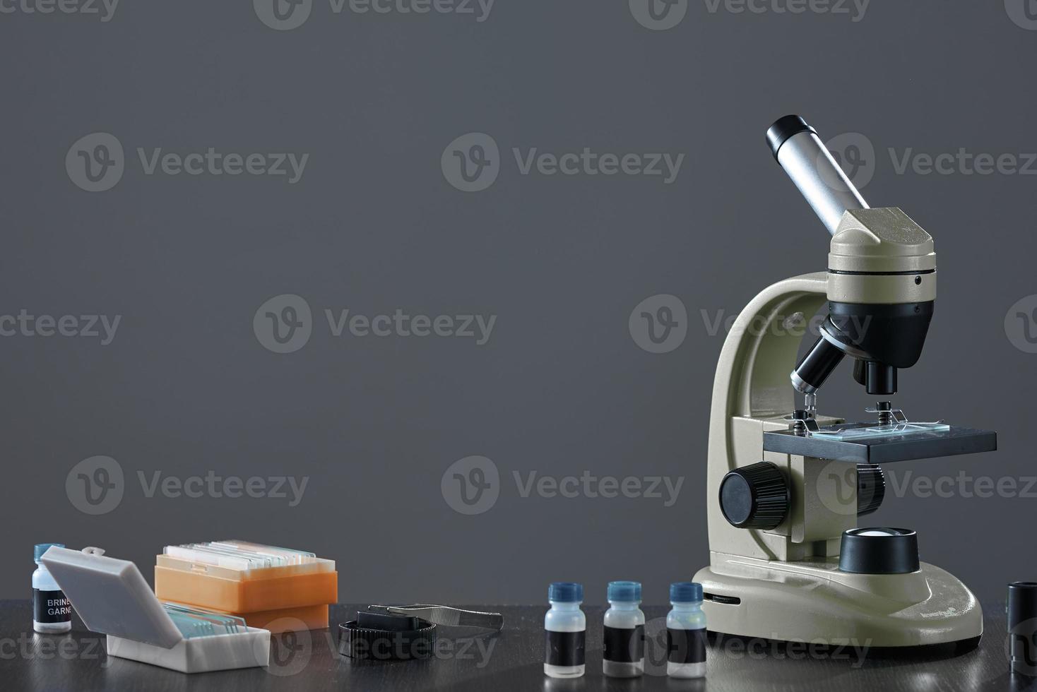 Microscoop en verschillende preparaten op tafel op een grijze achtergrond. foto