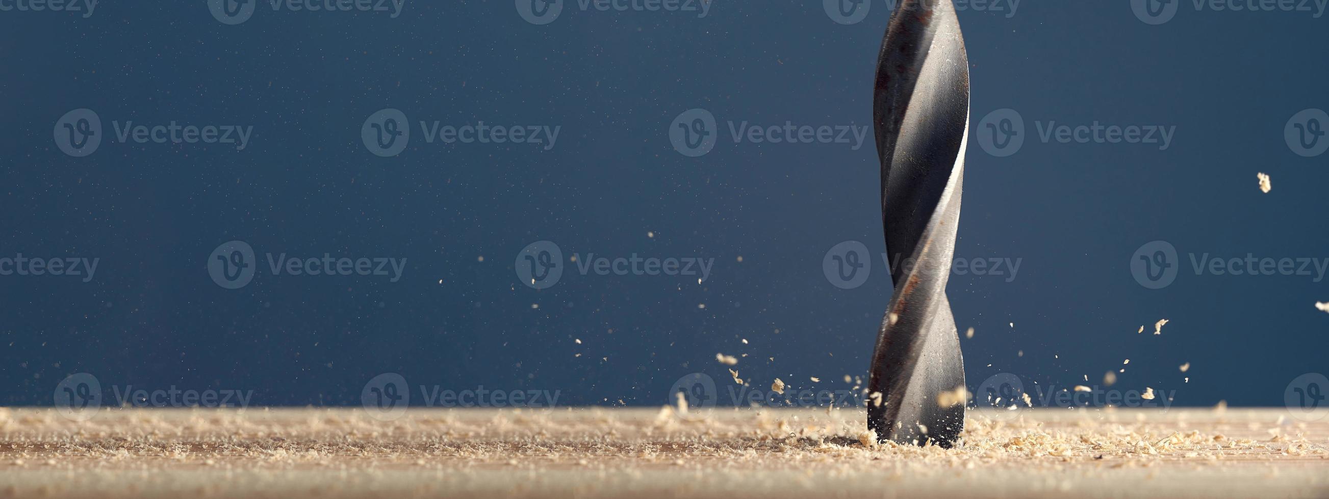 metalen natte boor maakt gaten in houten oppervlak op industriële boormachine met schaafsel op grijze achtergrond. foto met kopie ruimte.