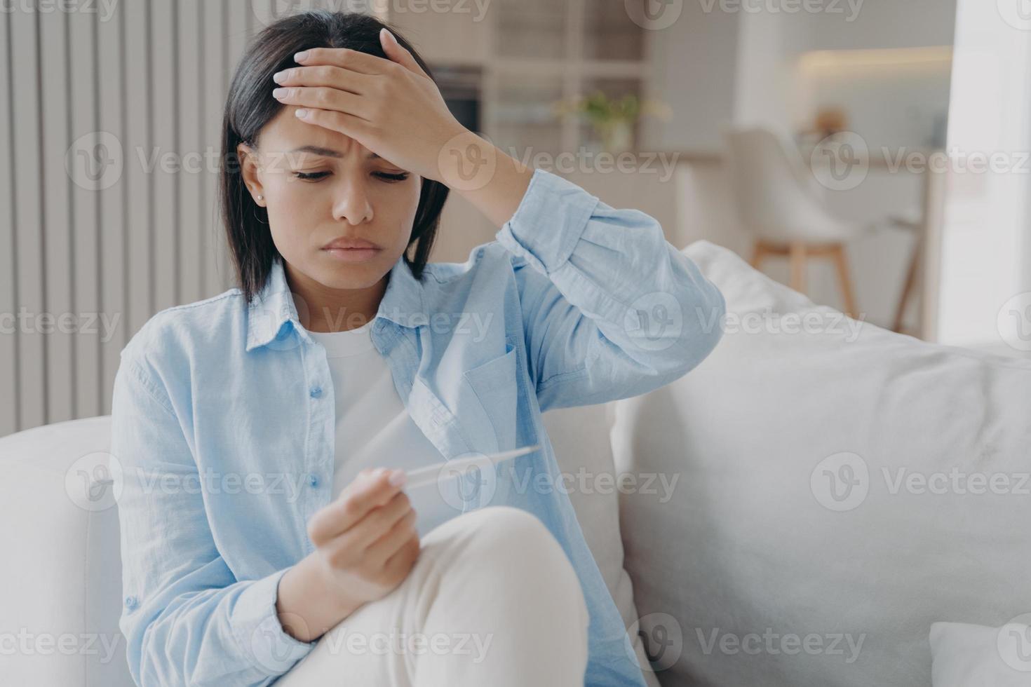 onwel slaperige vrouw onderzoekt de temperatuur en raakt het hoofd aan. vermoeidheid door virusinfectie. foto