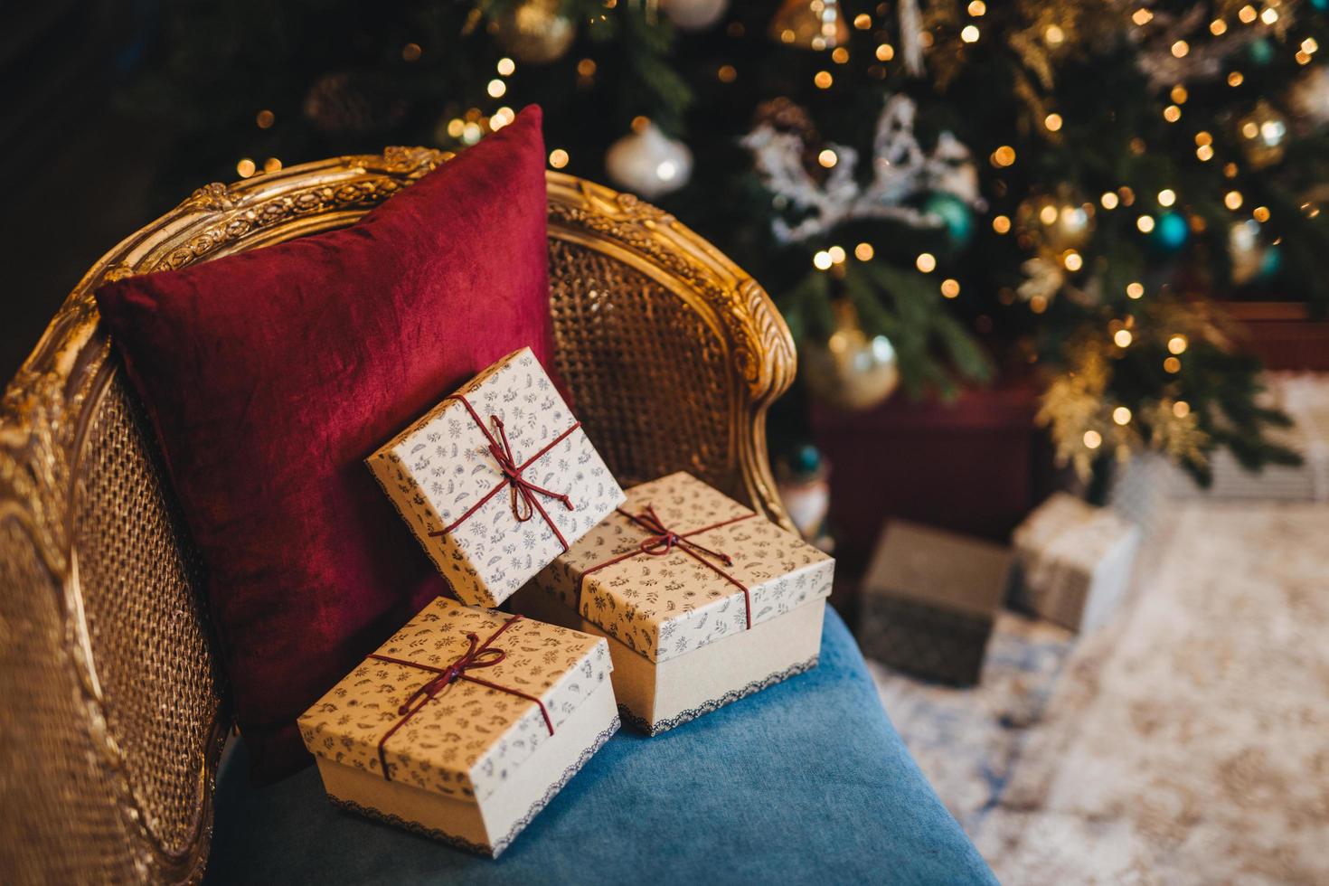 drie verpakte huidige dozen op fauteuil in de buurt van de kerstboom. ontwerp of idee voor ansichtkaart. nieuwjaarssamenstelling met versierde dennenboom en geschenken. majestueuze sfeer. feestelijke gebeurtenis foto