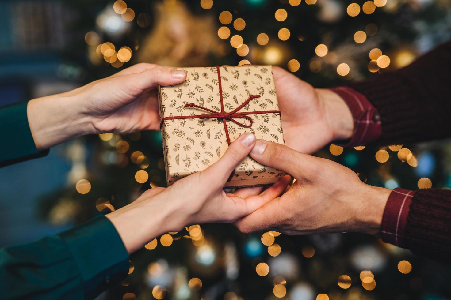 verpakte doos in handen van de vrouw en de man. aanhankelijke man feliciteert zijn vrouw met het nieuwe jaar, presenteert haar geschenkdoos voor de feestdagen, staat tegen de versierde kerstboom. vakantie concept foto