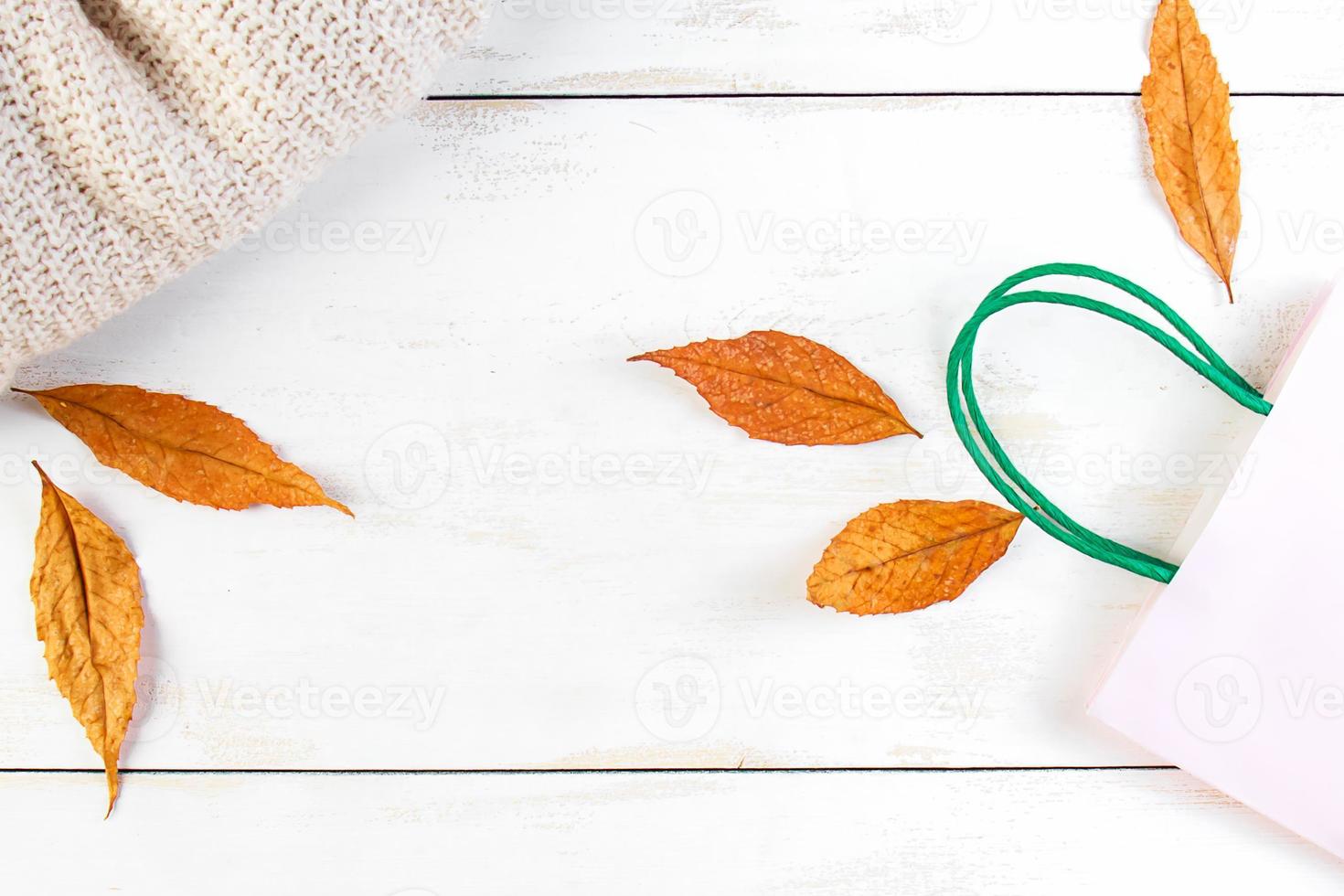 herfst korting en verkoop concept. papieren boodschappentas, gele bladeren en gebreide trui op witte houten achtergrond. foto