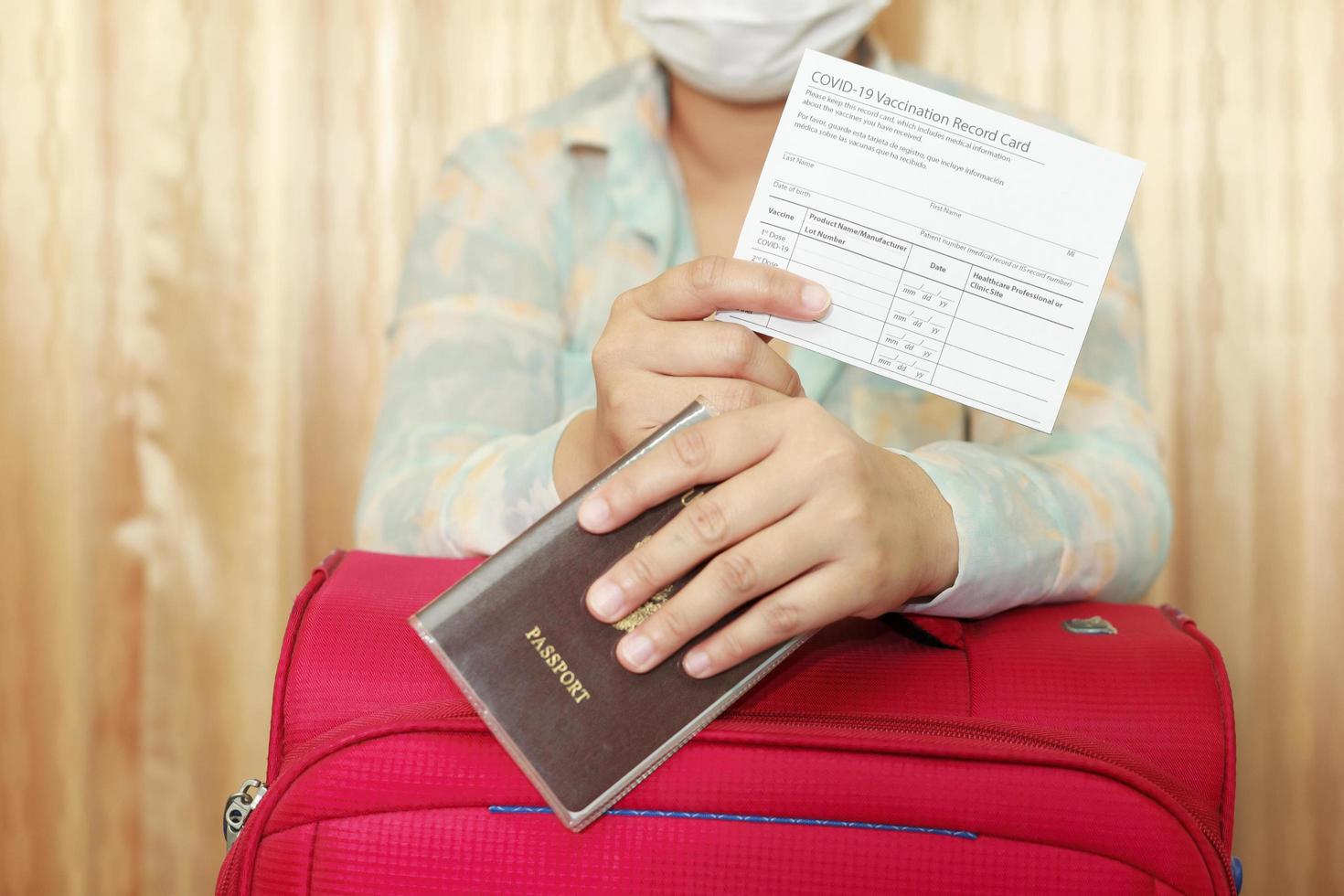 vrouw in reiskleding met een medisch masker met covid-19 vaccinatiekaart en paspoort en roze koffer. reisconcept met vaccinatie. foto