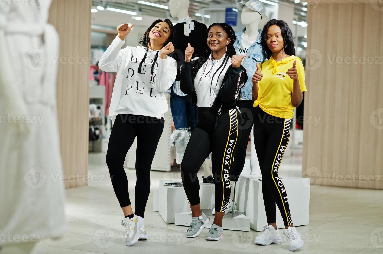 drie Afro-Amerikaanse vrouwen in trainingspakken winkelen en duim opdagen bij sportkleding winkelcentrum tegen mannequin. sport winkel thema. foto