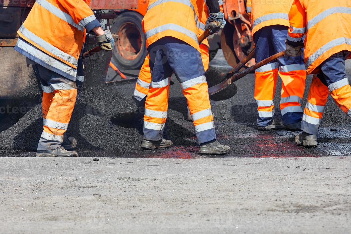 een wegenwerker strooit vers asfalt met schoppen over het reparatiegebied om een weggedeelte te repareren. foto