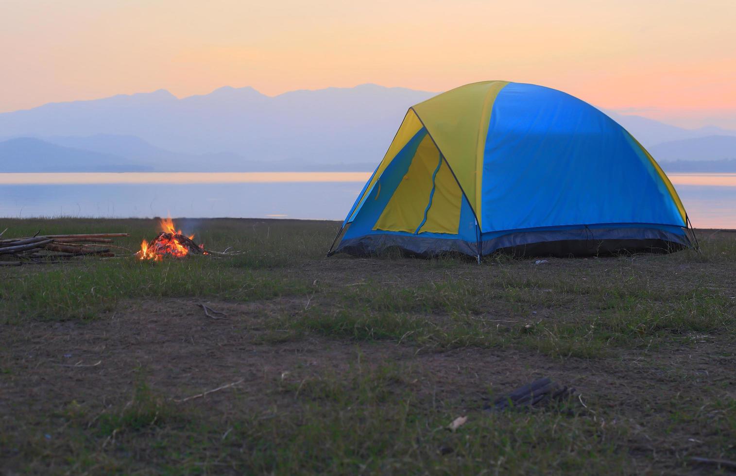 tent en kampvuur bij zonsondergang, naast het meer foto